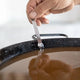 El Paeller Paella Broth Measurer - hand placing the measurer on the rim of a pan filled with broth
